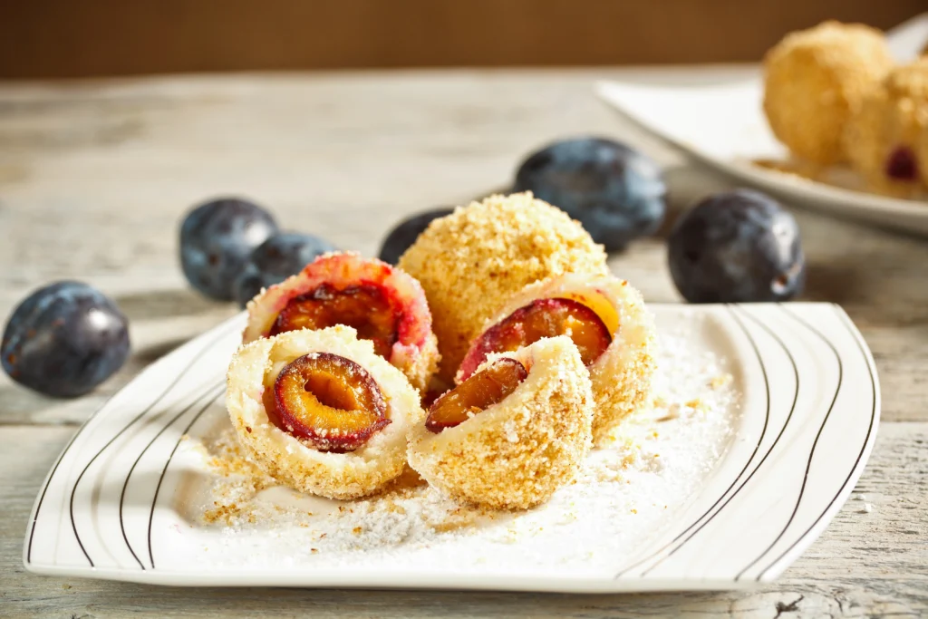 Hungarian sweet plum dumplings (szilvás gombóc) rolled in toasted breadcrumbs and powdered sugar on plate — traditional homemade dessert popular in Hungary.