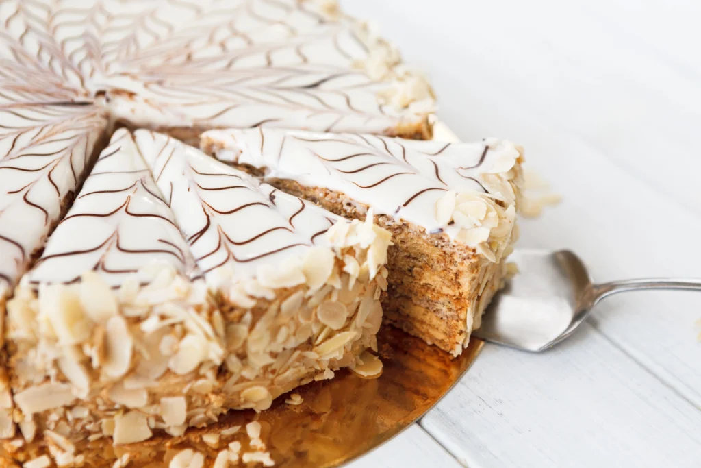 Hungarian Eszterházy Torta cake sliced on white plate with almond garnish and fondant top — classic layered walnut dessert popular in Hungary.