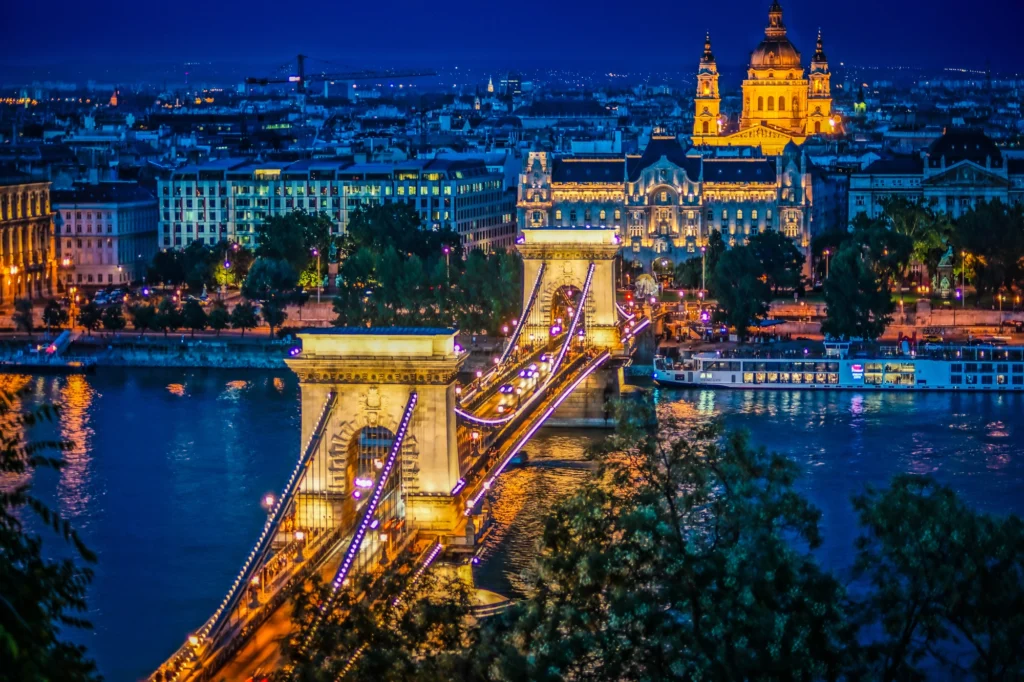 Night view of Budapest’s Chain Bridge illuminated against the Danube, with St. Stephen’s Basilica and city lights in the background—an iconic evening cityscape