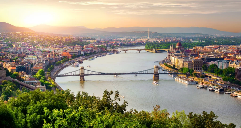 Panoramic sunset view over the Danube River with the Chain Bridge and Parliament, capturing both Buda and Pest districts in golden light—an iconic Budapest cityscape