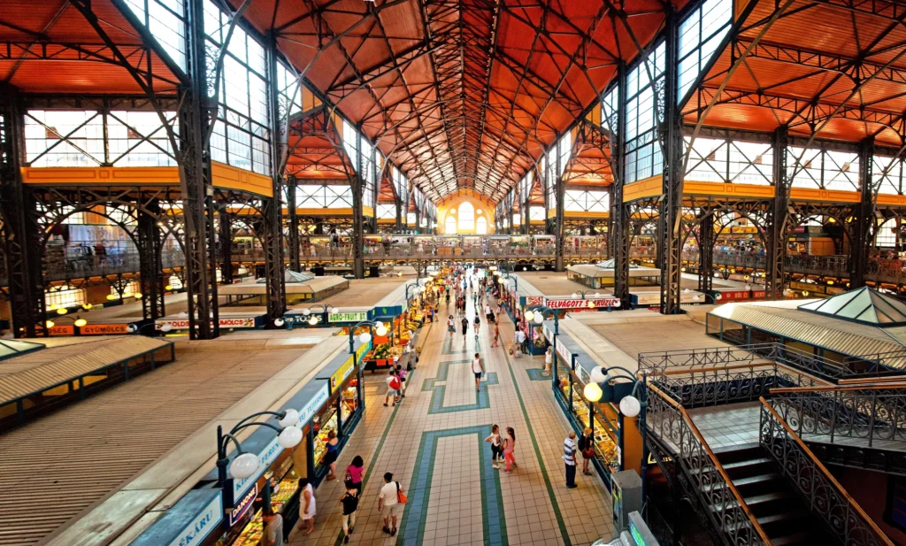 Interior view of Budapest’s Great Market Hall with its soaring iron roof, vibrant vendor stalls, and bustling shoppers—a lively hub for Hungarian food, crafts, and souvenirs.